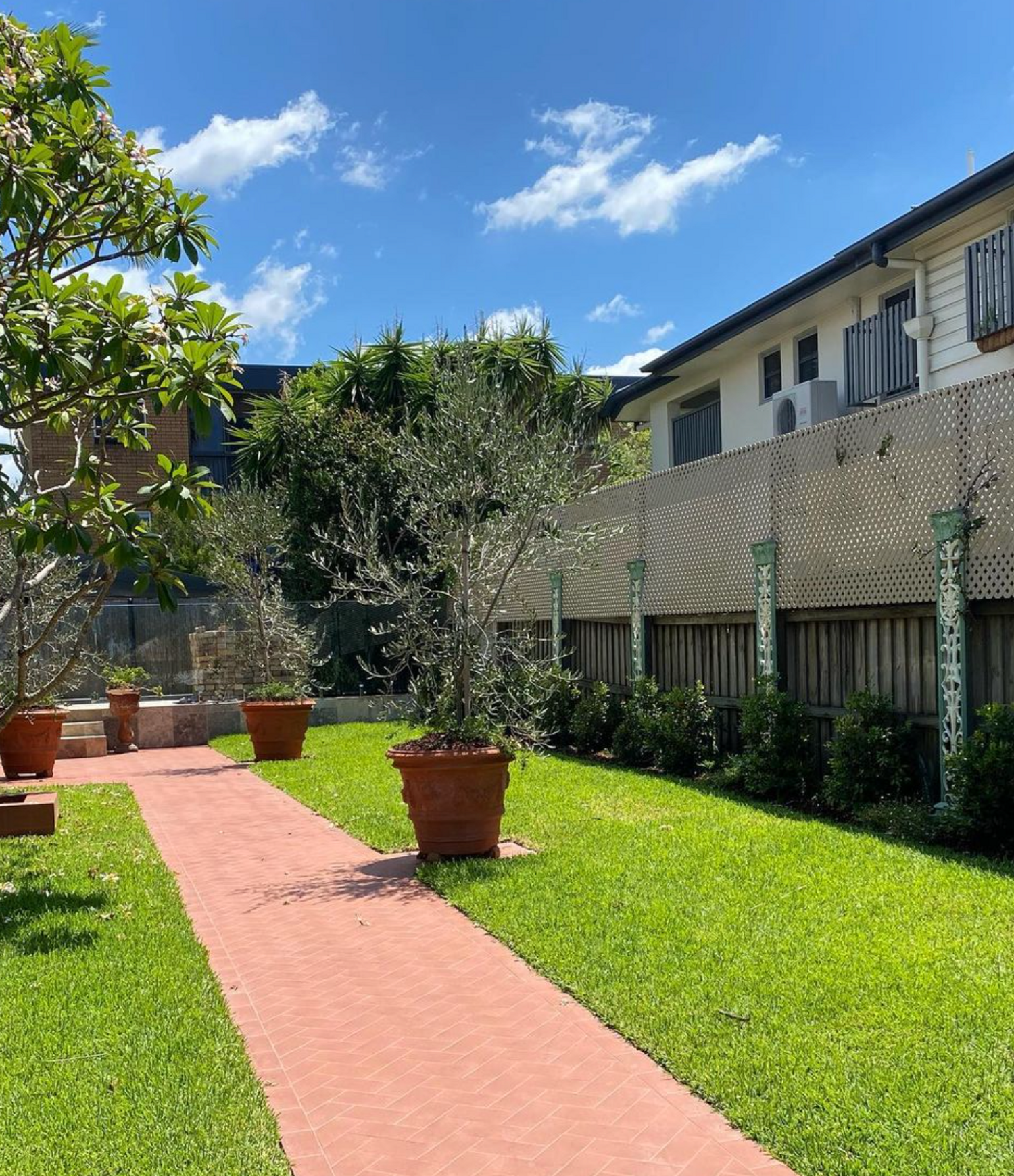 Brick pathway with potted plants and lush green lawn in New Farm